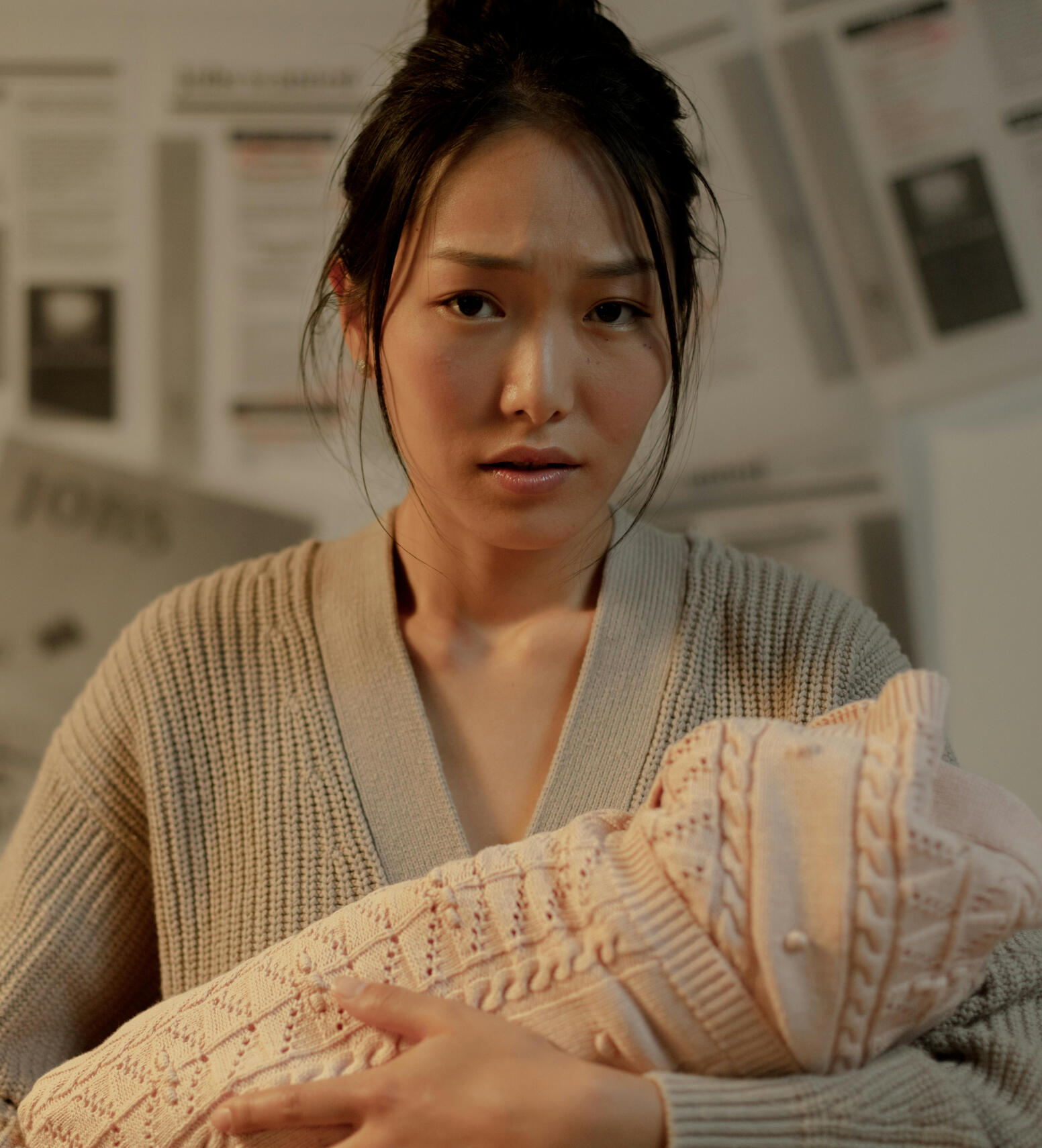 worn out mom with messy hair and a tired expression on her face holding her baby that is wrapped in a blanket