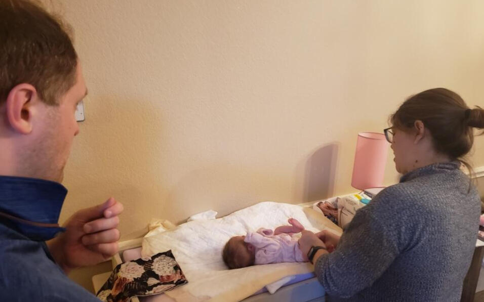 me teaching a father how to diaper his daughter. She is laying on her changing table and I am standing right next to the baby as dad watches