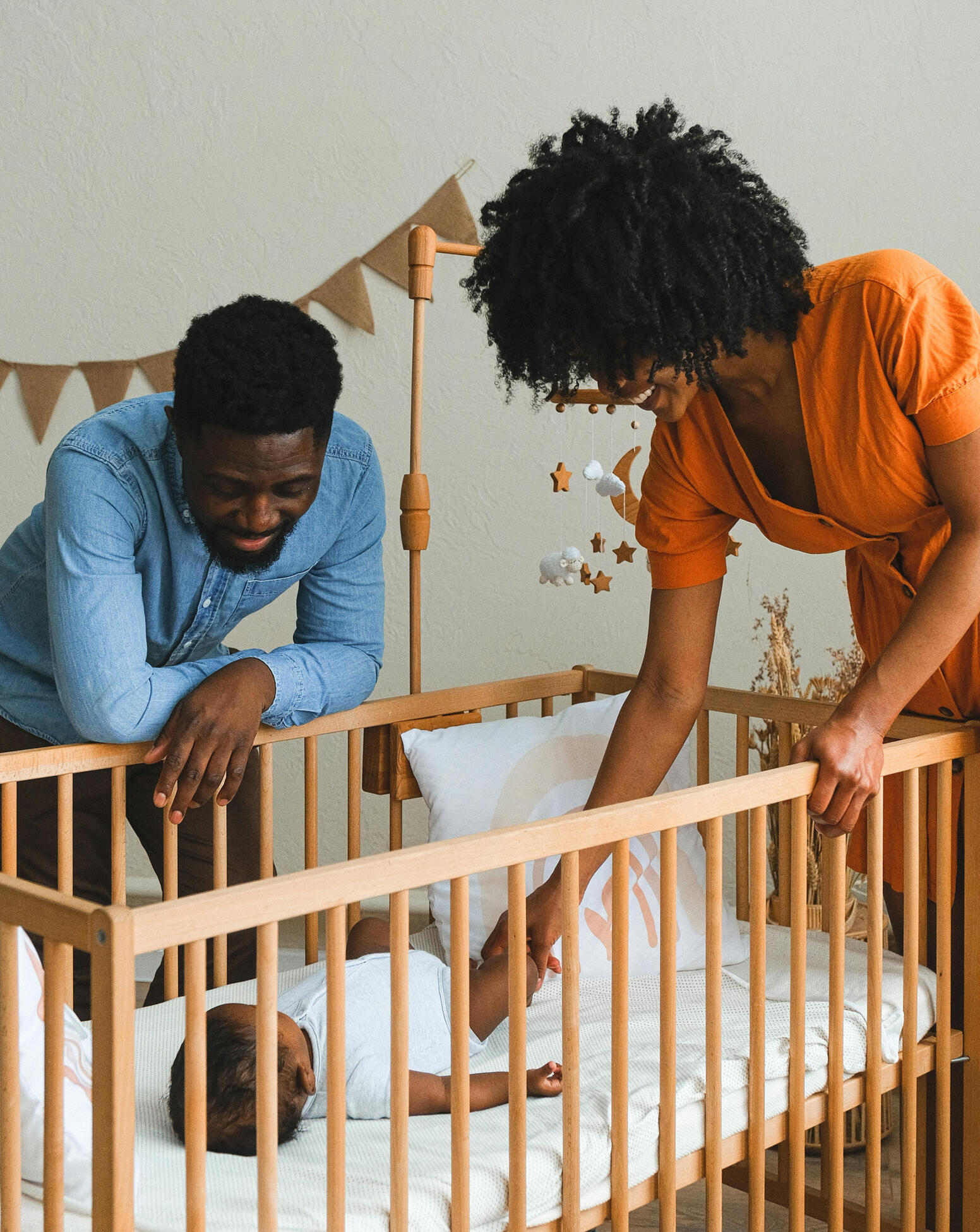 Mom and dad are leaning over a crib and mom is reaching in to comfort her newborn baby